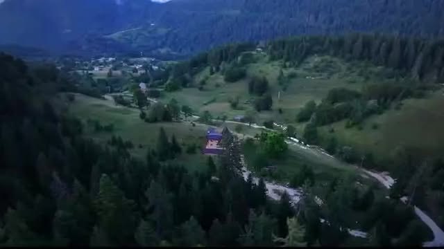 Pogled iz vazduha na zelenu planinsku dolinu sa vilom i četinarskom šumom